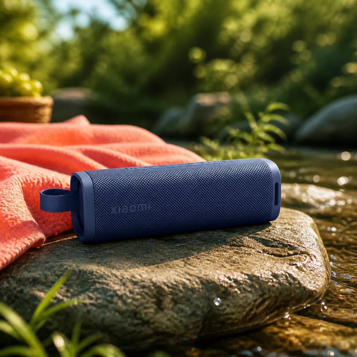 اسپیکر آبی Xiaomi Sound Outdoor روی سنگ کنار جوی آب و زیر نور تابستانی