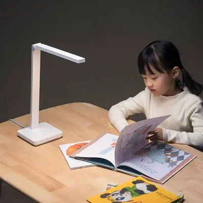 مطالعه کودک با چراغ شیائومی Mijia Table Lamp Lite دختر در حال ورقزدن کتاب تصویری روی میز چوبی کنار چراغ روشن Mijia Table Lamp Lite